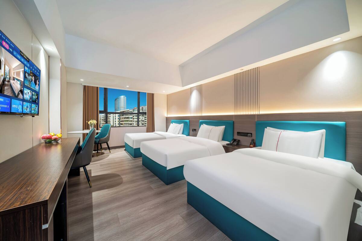 Habitación de hotel con dos camas, un escritorio y un televisor que muestra varios canales.
