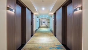 A hotel hallway with a carpeted floor, wooden doors, and illuminated room numbers. - Guangzhou Meigang Hotel (Guangzhou)