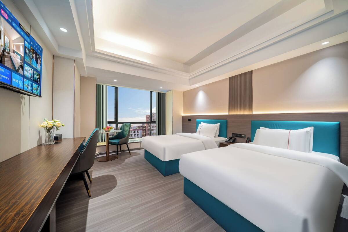 Habitación de hotel con dos camas, un escritorio, una silla, un televisor y vista a la ciudad.