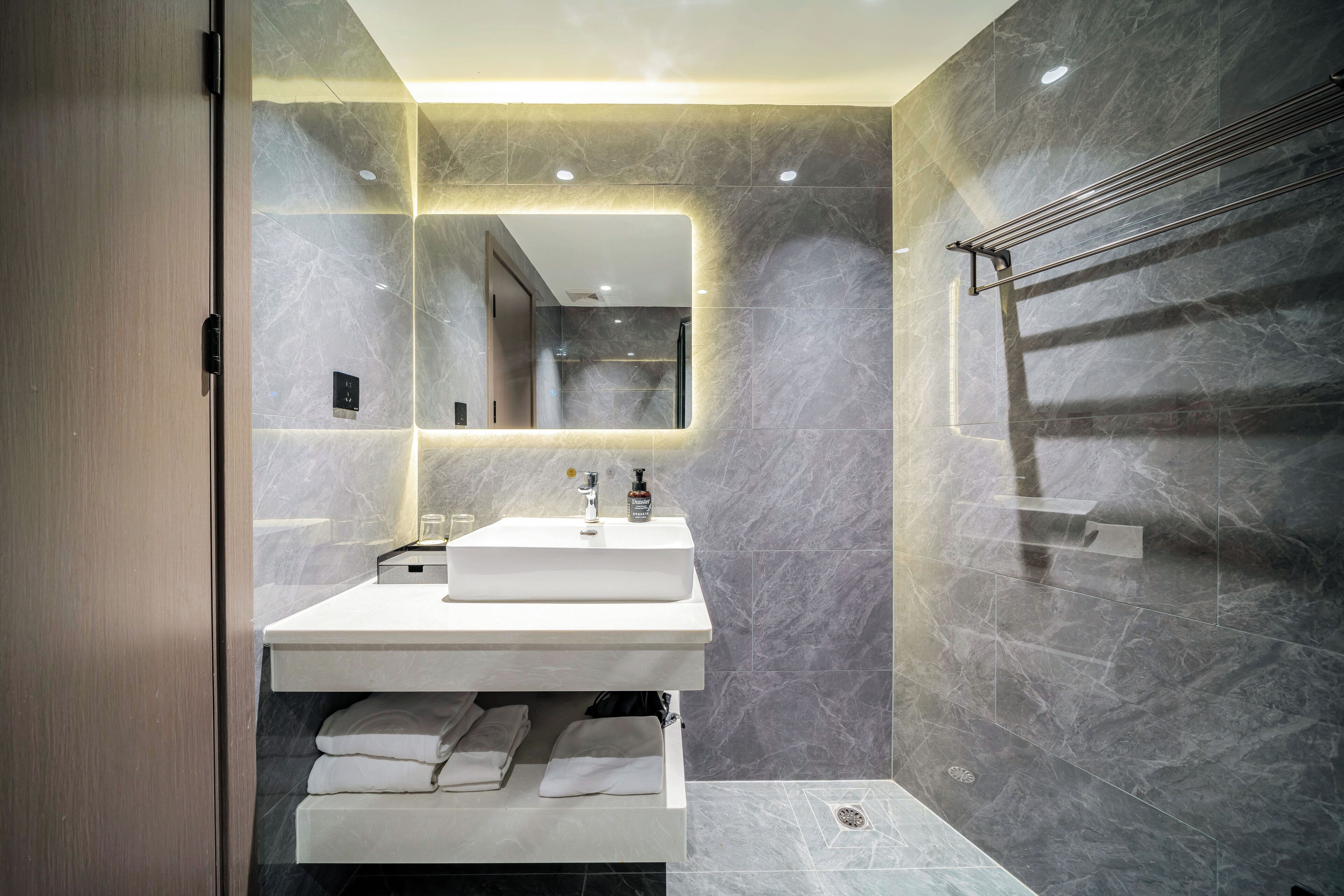 A modern bathroom with a large mirror, a white sink, and a towel rack.