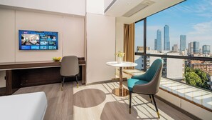 A hotel room with a large window, a flat-screen TV, a bed, a desk, and a chair. - Guangzhou Meigang Hotel (Guangzhou)