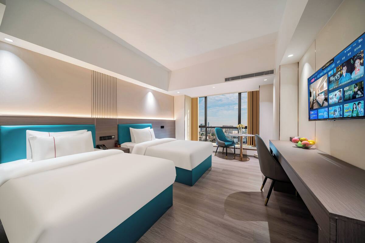 Habitación de hotel con dos camas, un escritorio, una silla, un televisor y vistas a la ciudad.