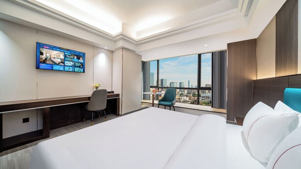 A hotel room with a large bed, a desk, a chair, a TV mounted on the wall, and a view of the city through large windows. - Guangzhou Meigang Hotel (Guangzhou)