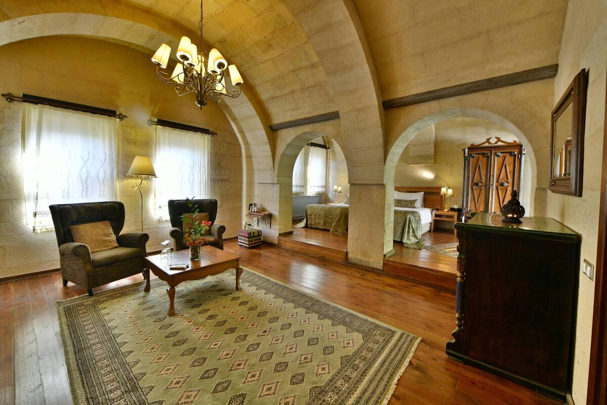 A spacious living room with wooden flooring, a patterned rug, a sofa, a coffee table, and a chandelier.