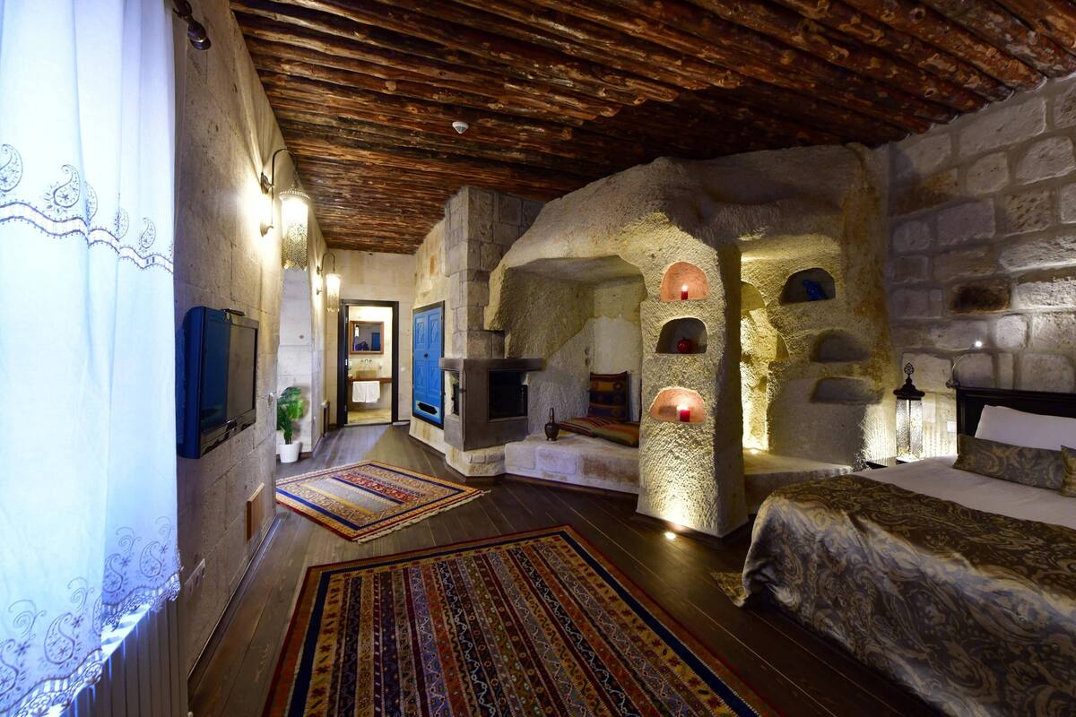 A rustic room with stone walls, a wooden ceiling, and a bed with patterned bedding.