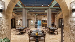 Uma ampla sala de jantar com paredes de pedra, vigas de madeira e uma mesa central posta para refeição.