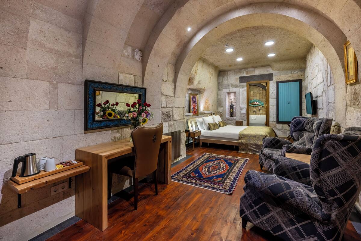 A cozy room with a wooden desk, a comfortable sofa, a bed, and a stone wall.