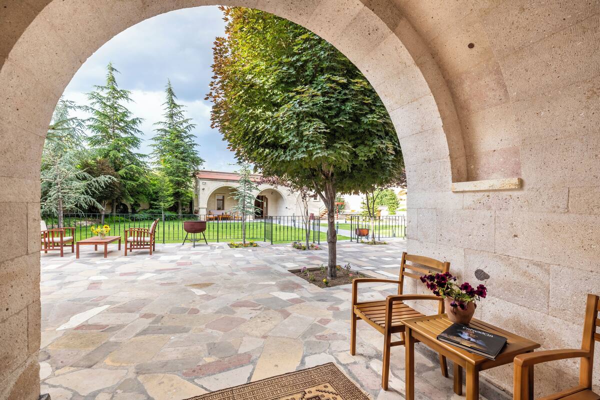 An outdoor patio area with stone flooring, wooden furniture, and a view of a building in the background.