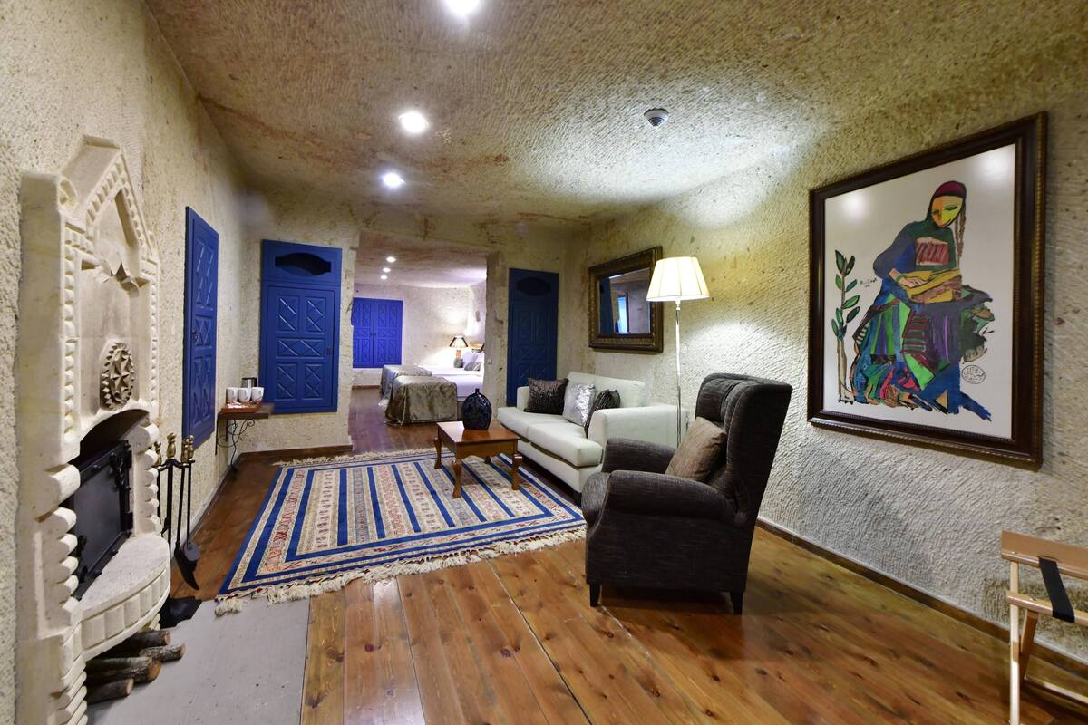 A room with a fireplace, a sofa, a chair, a blue rug, and a painting on the wall.