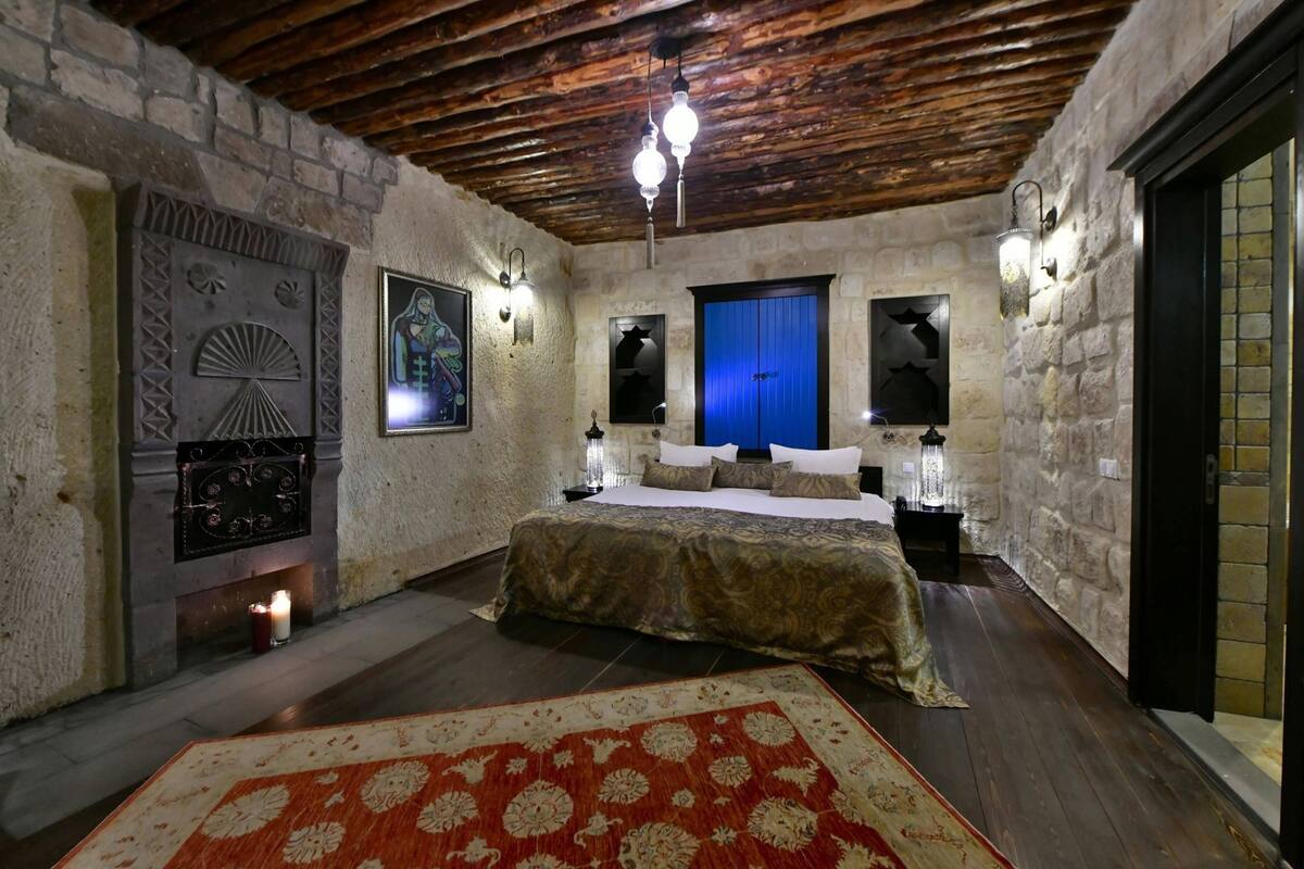 A bedroom with a bed, a fireplace, a rug, and stone walls.