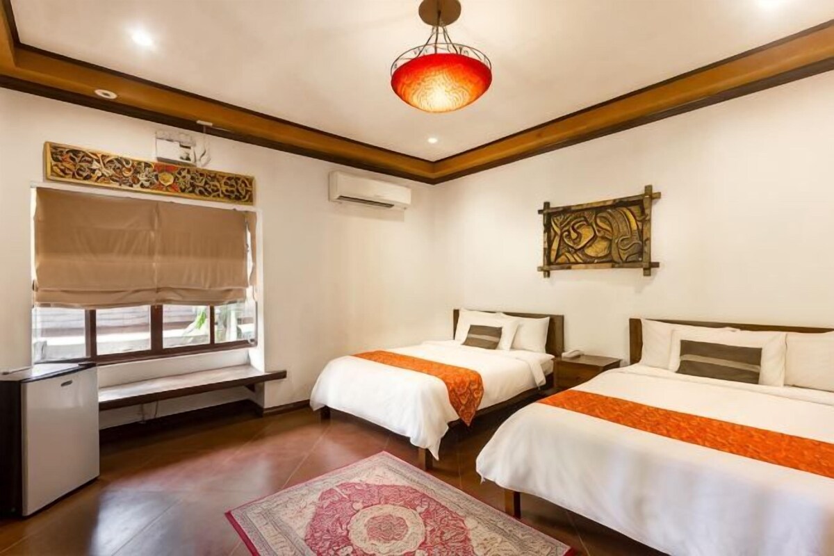 A hotel room with two beds, a desk, a window with a view, and a ceiling light fixture.