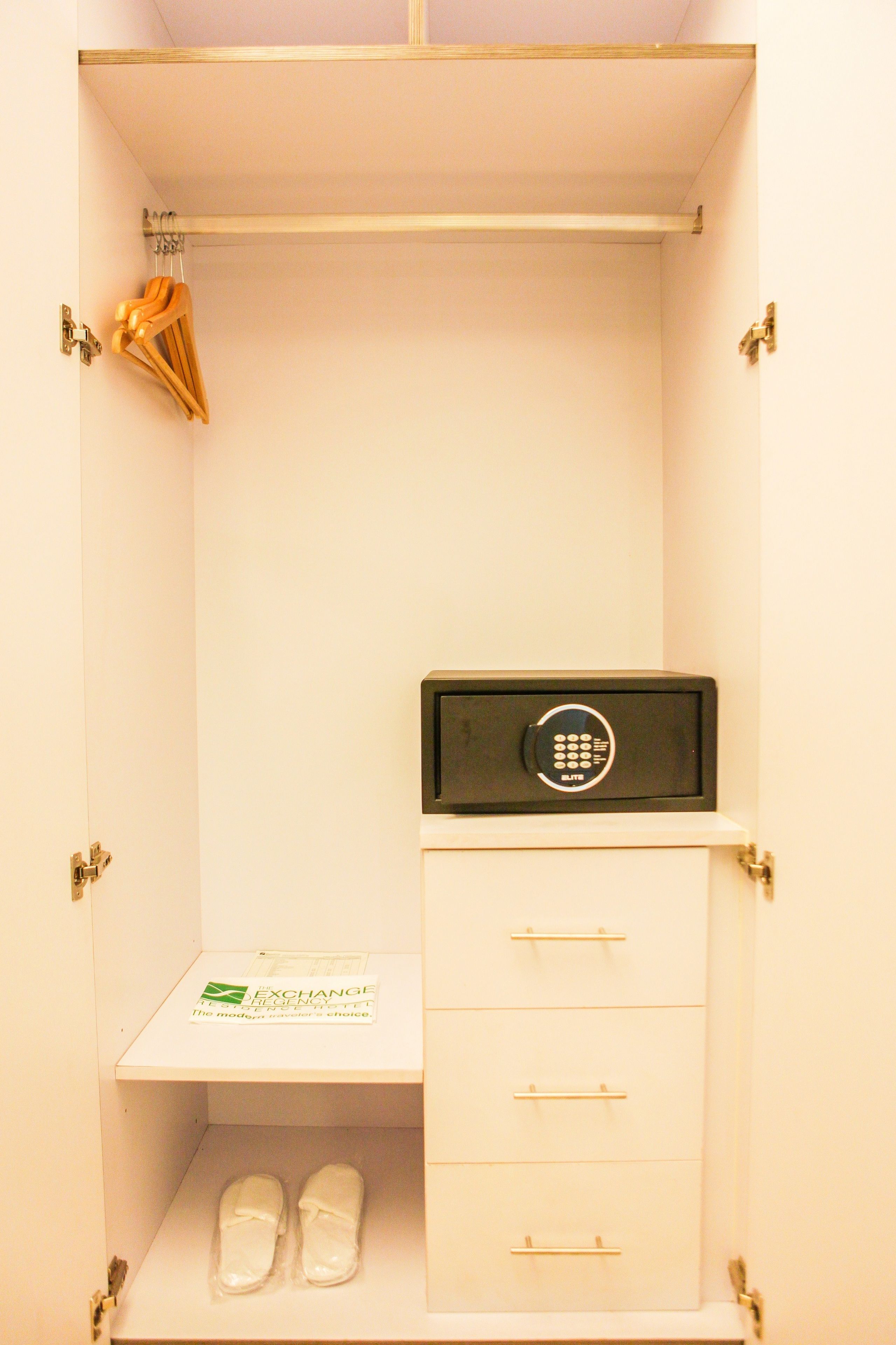 A white wardrobe with a black safe, a pair of slippers, and a hanging garment organizer.