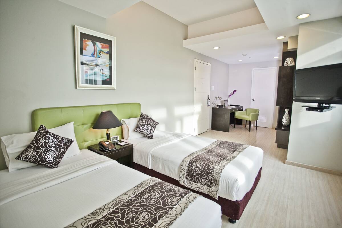 A hotel room with two beds, a desk, a television, and a painting on the wall.