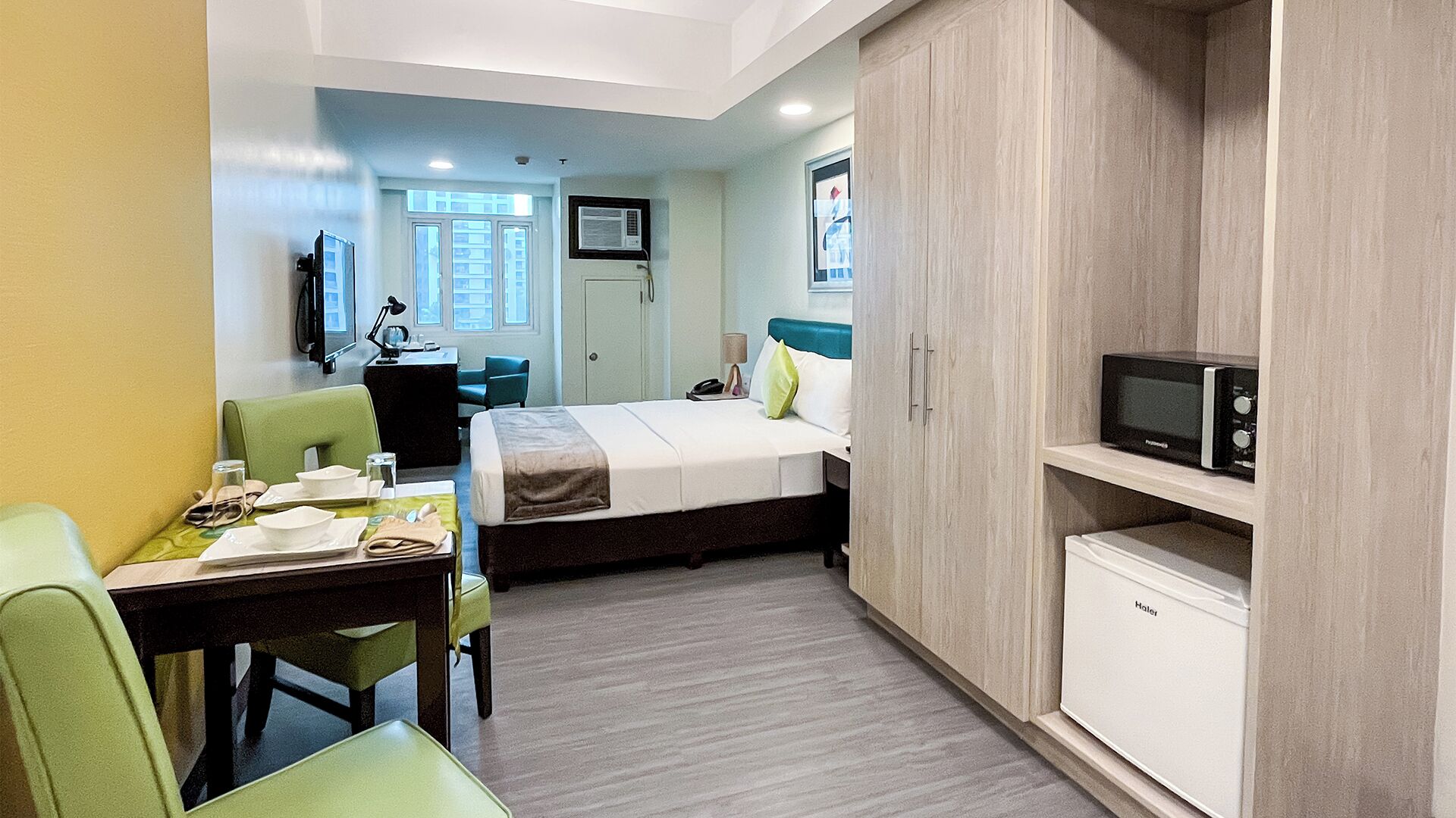 Une chambre d’hôtel compacte comprenant un lit, un bureau, une chaise, un four à micro-ondes et un mini-bar.