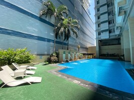 Una piscina con sillones de descanso y palmeras, rodeada por un edificio de diseño moderno.