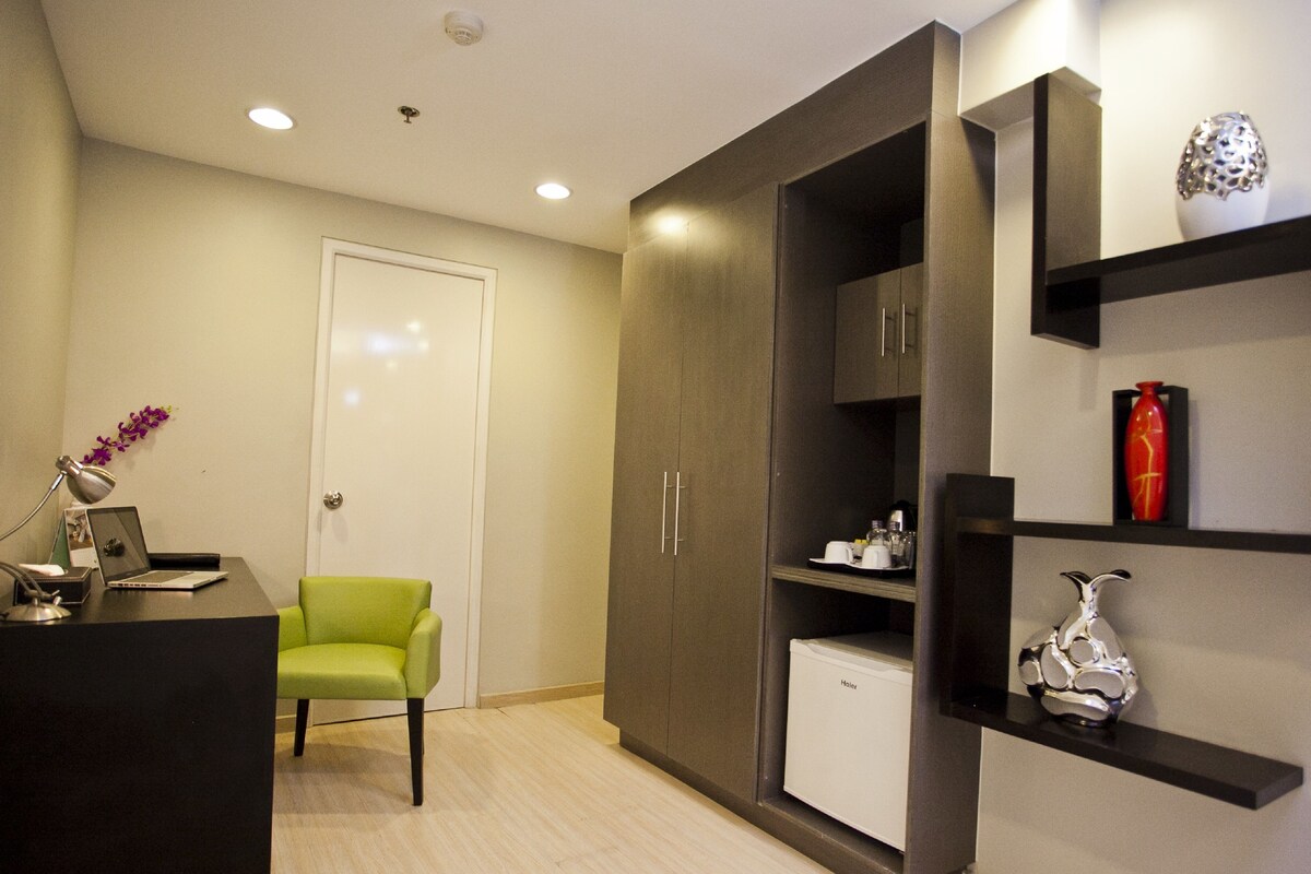 A modern room with a desk, chair, wardrobe, shelves, and a small refrigerator.