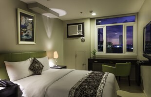 Habitación de hotel con cama, escritorio, silla y vista nocturna a la ciudad.