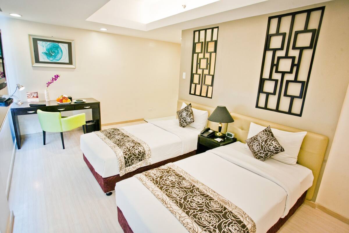 Une chambre d’hôtel avec deux lits, un bureau, une chaise et des œuvres d’art décoratives au mur.