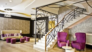 A modern interior with a curved ceiling, a staircase with a metal railing, a sofa with purple cushions, and two purple armchairs. - The Exchange Regency Residence Hotel (Pasig)