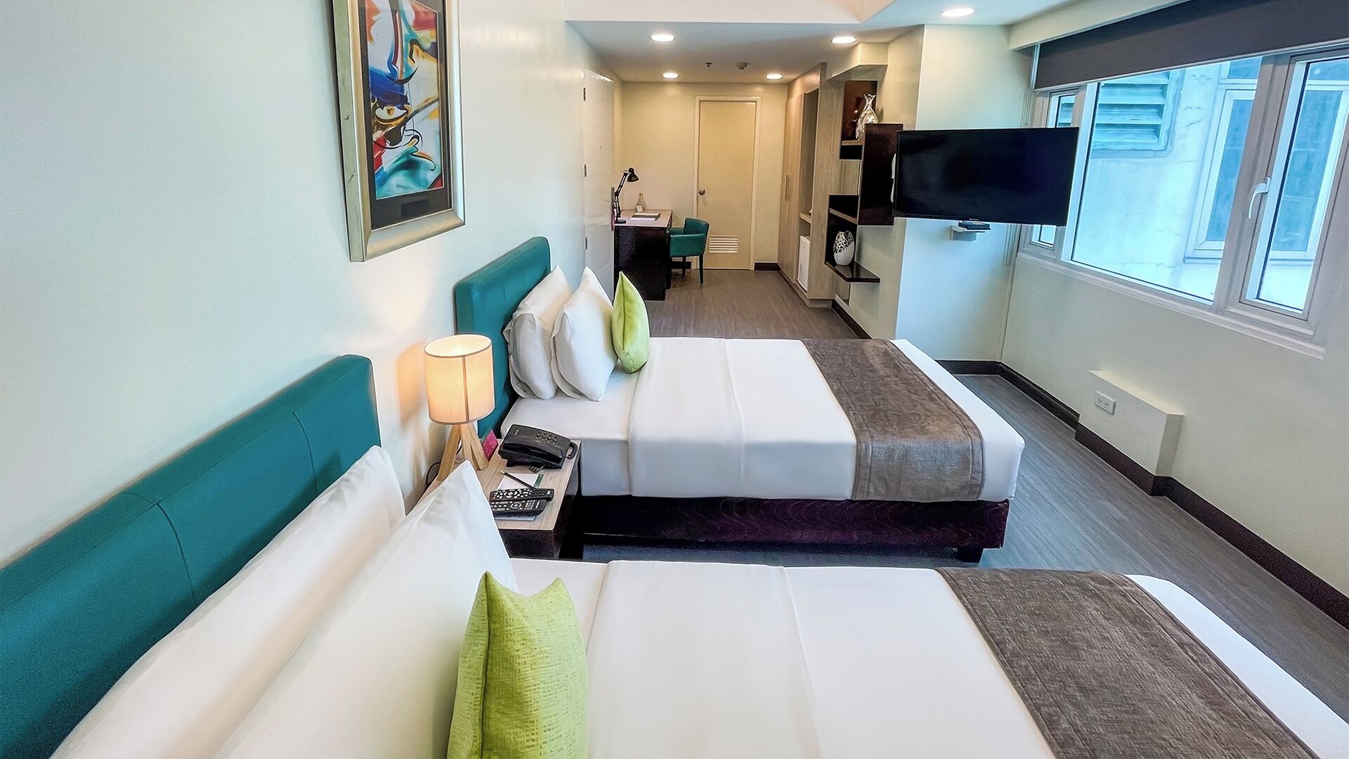 Habitación de hotel con dos camas, un escritorio, una silla, un televisor y una ventana.