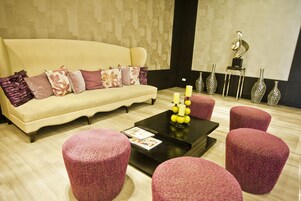 Una sala de estar moderna con un sofá color beige, otomanas rosadas, una mesa de centro negra y jarrones decorativos.
