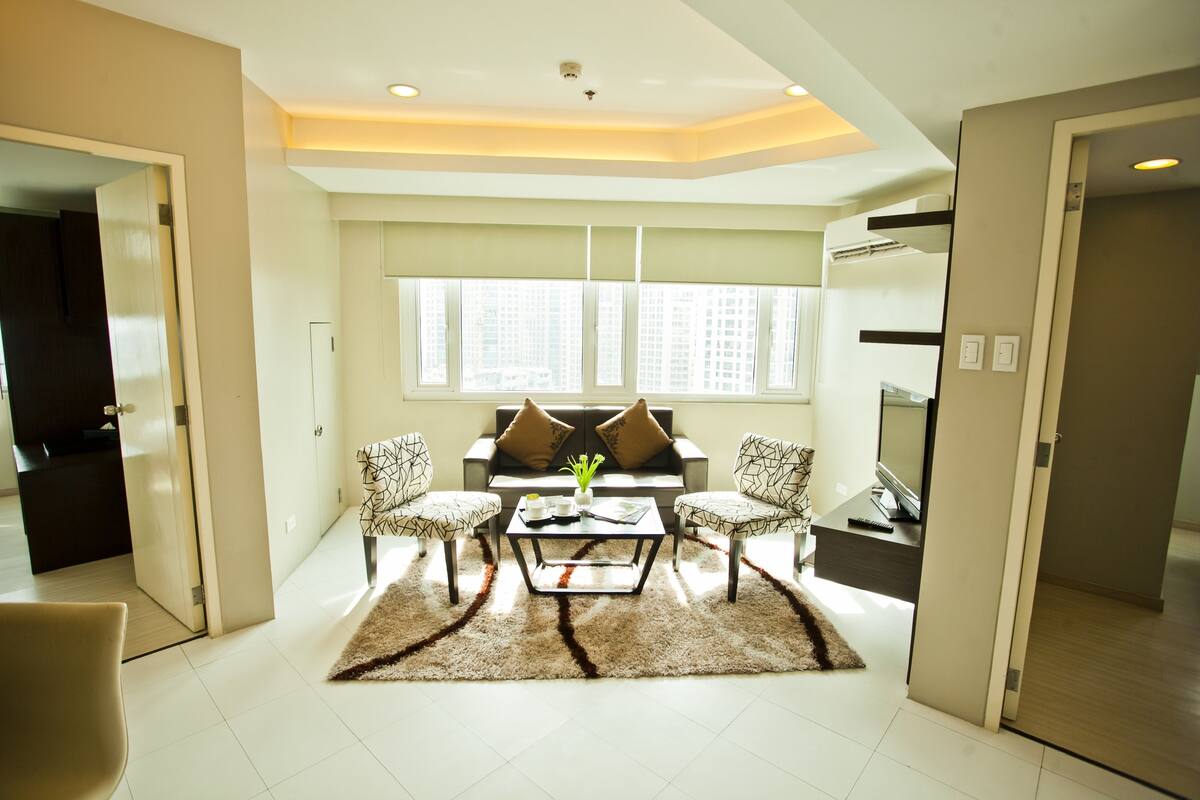A modern living room with a sofa set, two armchairs, a coffee table, and a large window with blinds.