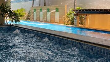 A pool area with a hot tub, a water feature, and a view of a building with a modern design.