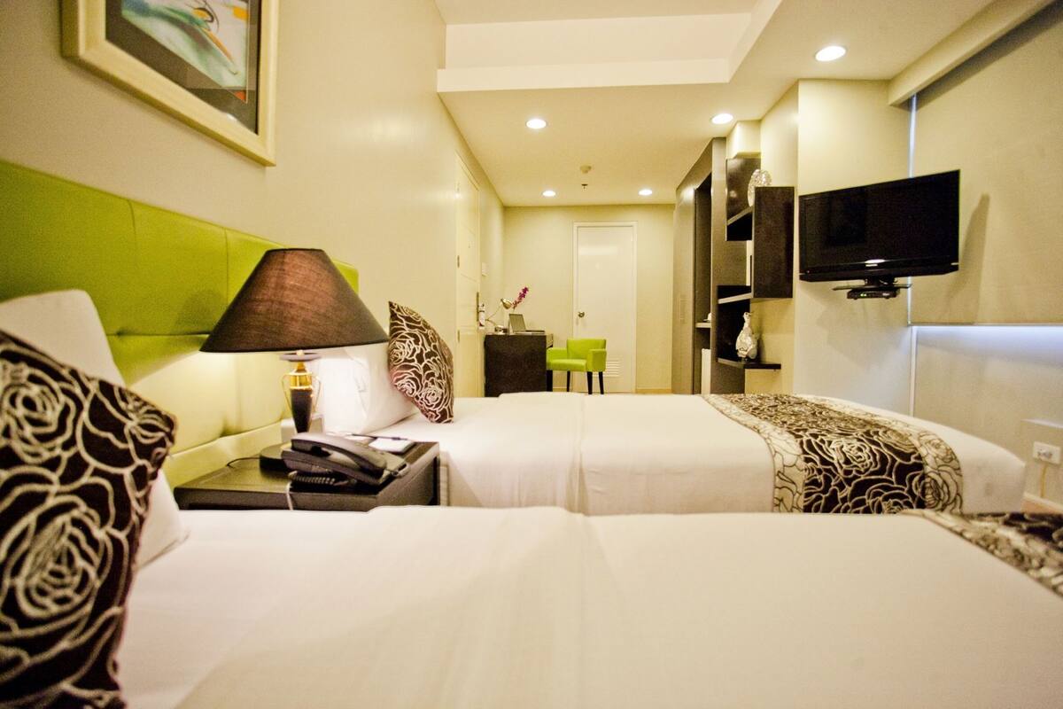 A hotel room with two beds, a desk with a lamp, a television, and a chair.