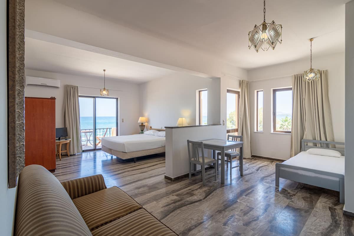 A hotel room with a bed, a desk, a chair, a sofa, and a view of the sea.