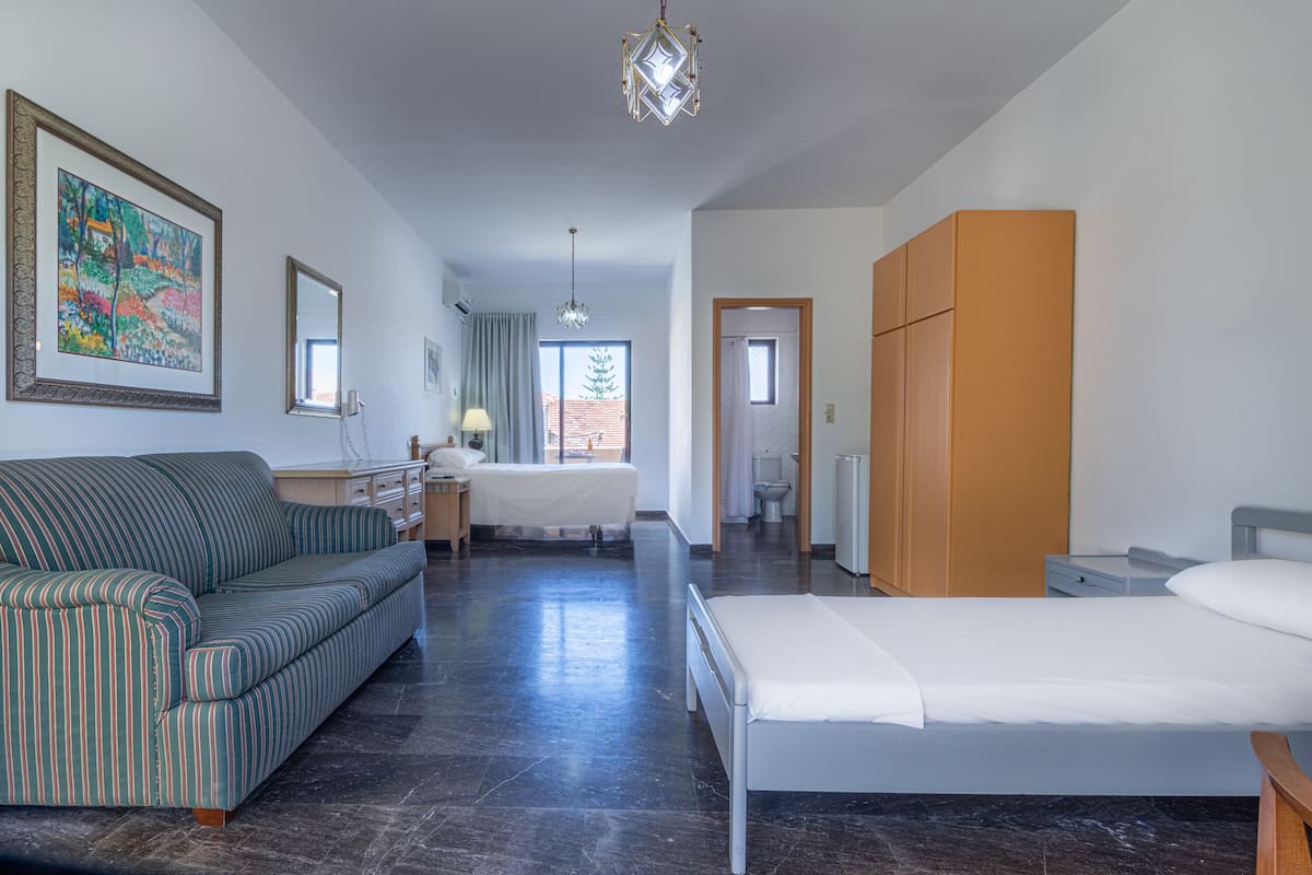 A hotel room with a bed, a sofa, a desk, a mirror, and a painting on the wall.