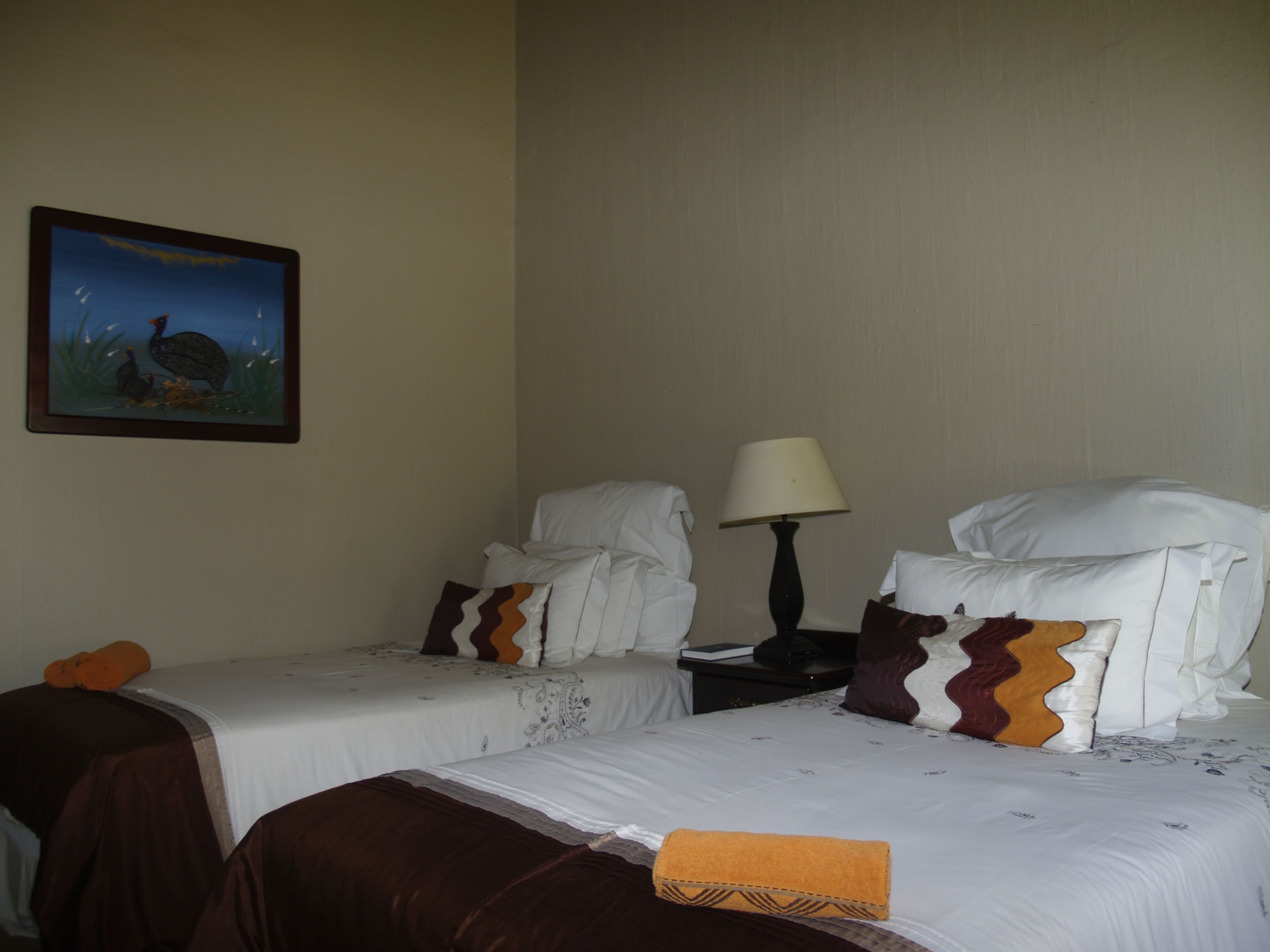 A hotel room with two beds, a nightstand with a lamp, and a painting on the wall.