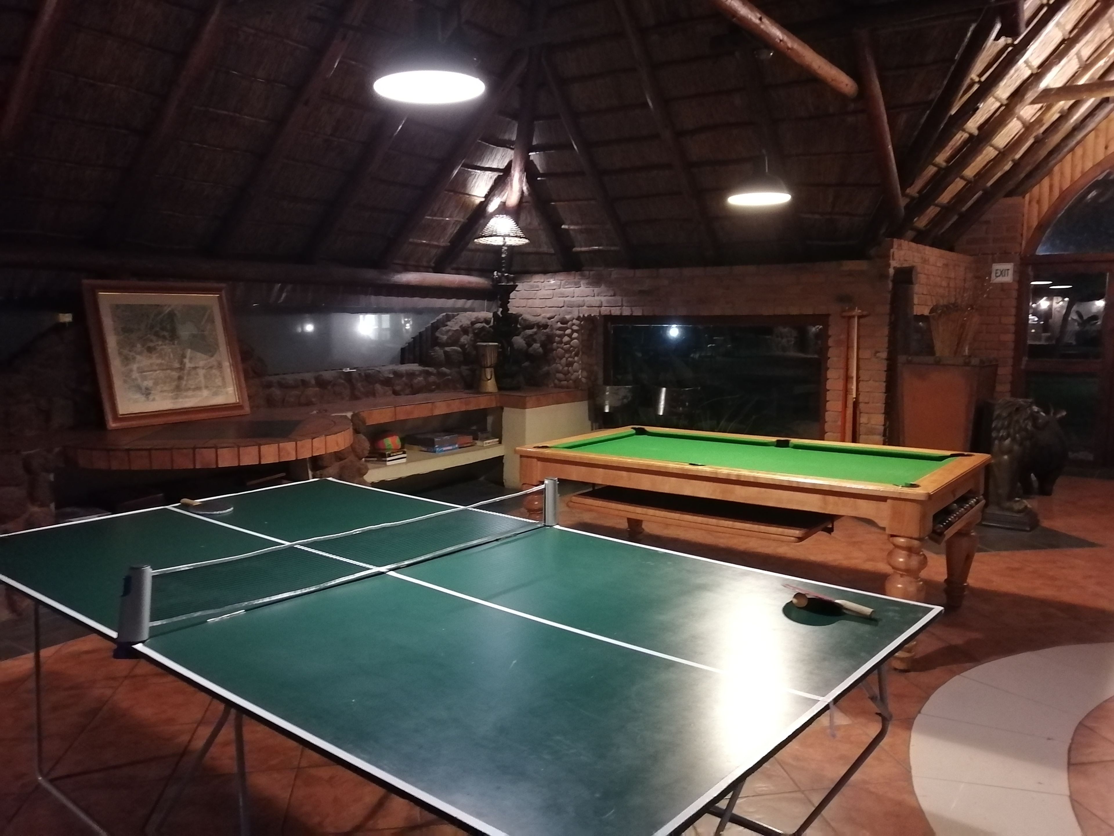 Een biljarttafel en een tafeltennistafel in een ruimte met een rustiek houten plafond en bakstenen muren.