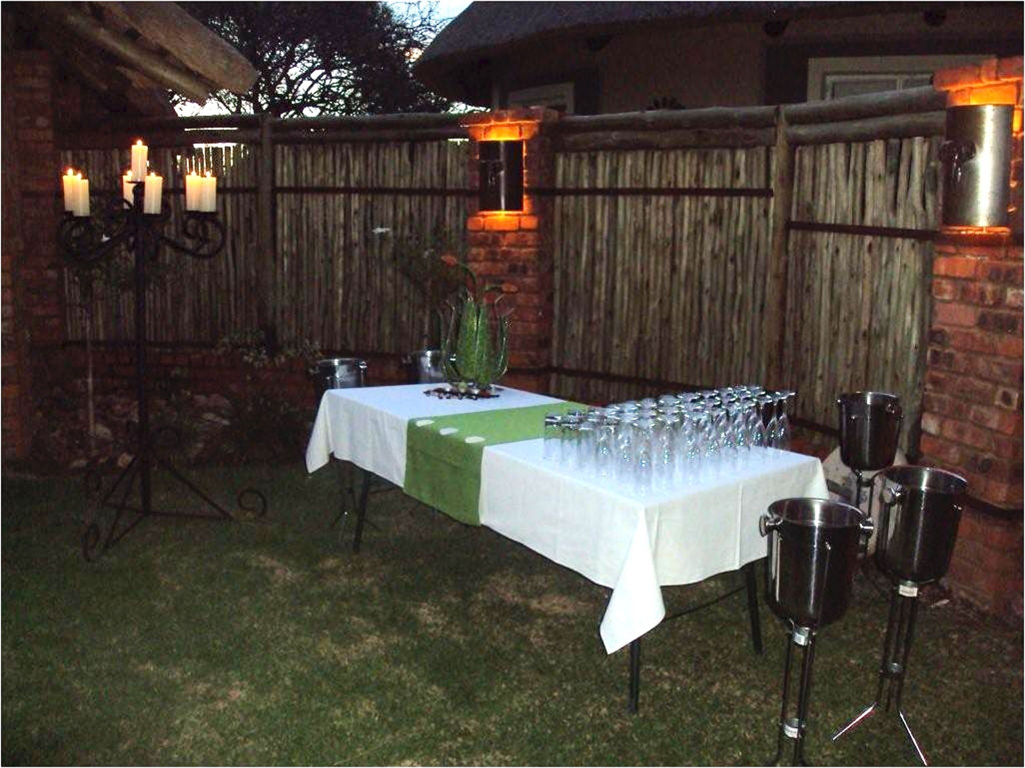 Un área de comedor al aire libre con una mesa preparada para una comida, rodeada por una valla de madera y un muro de ladrillo.