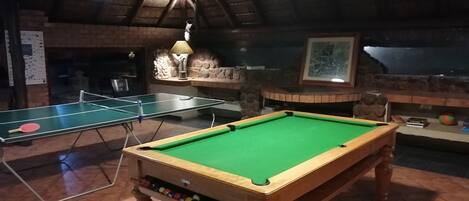 Une salle de billard équipée d’une table de billard, de deux tables de ping-pong et d’une cheminée en pierre.