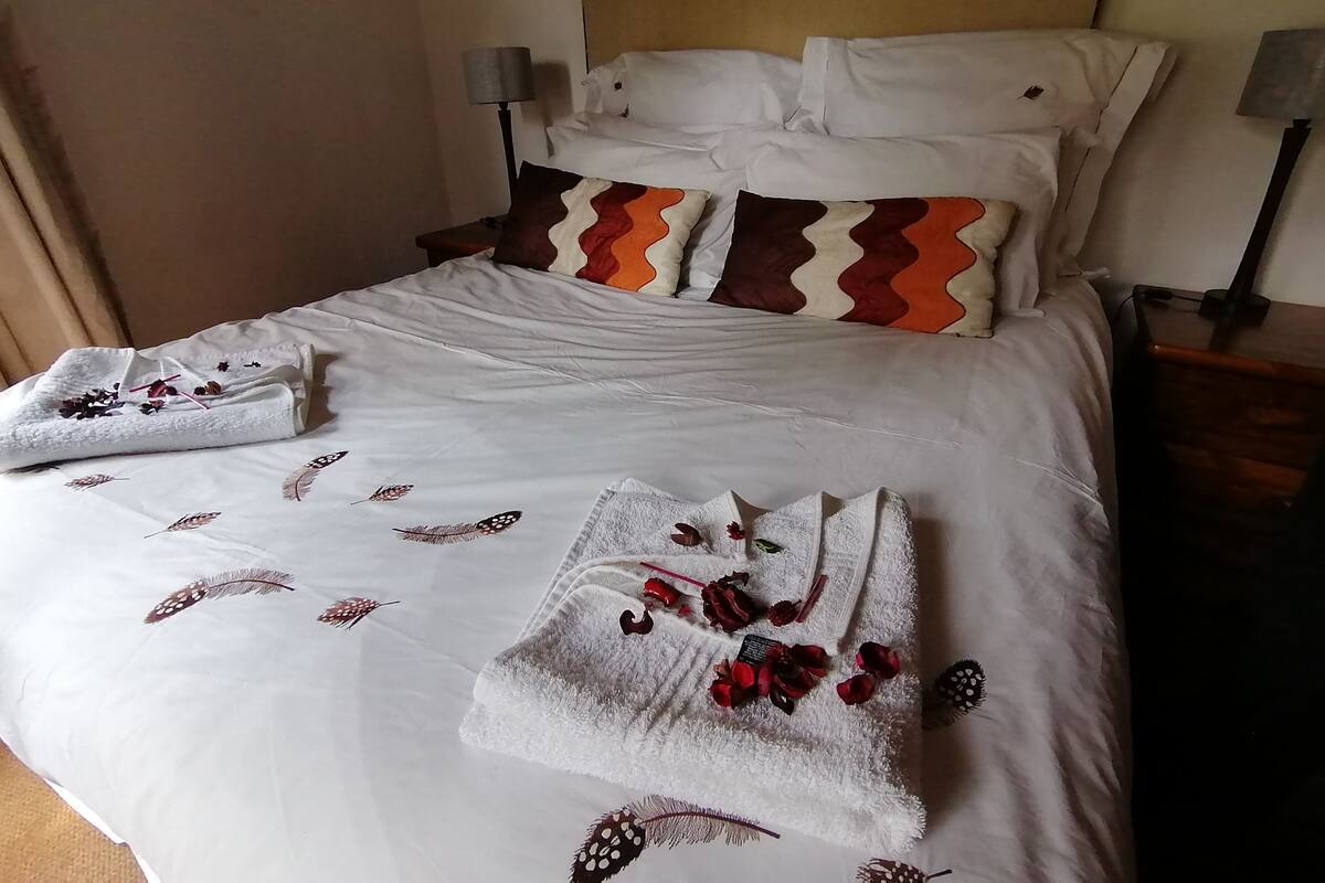 Ein ordentlich bezogenes Bett mit weißen Leinen, dekorativen Kissen und Handtüchern mit Blumenmuster.