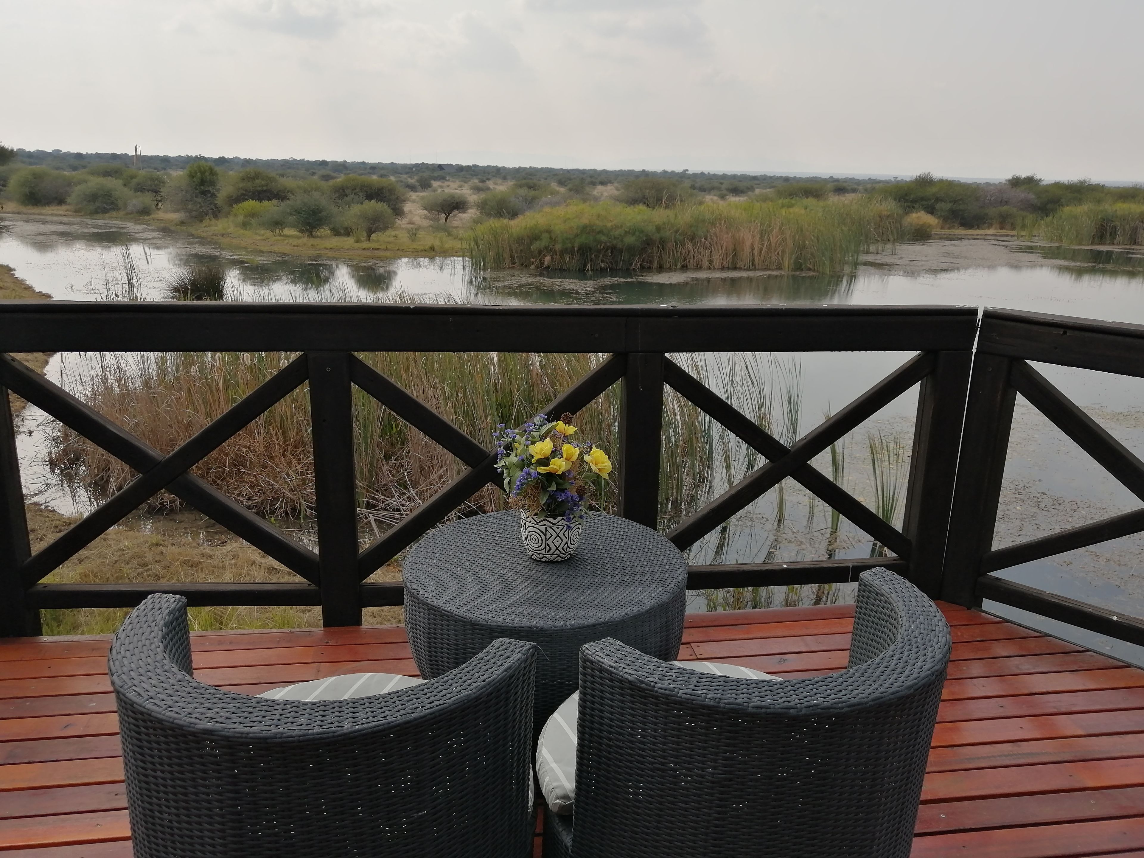 A deck with wicker furniture overlooking a body of water and vegetation.
