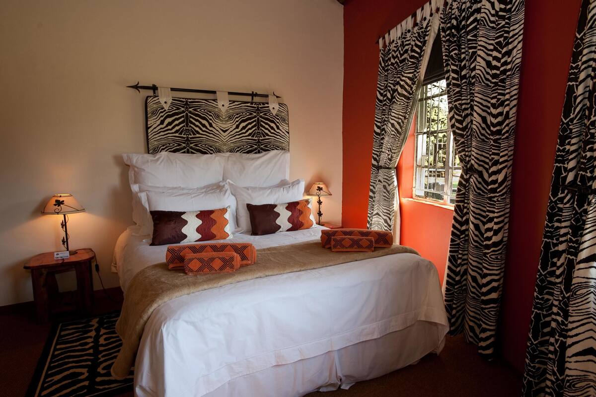 Ein Bett mit weißer Bettwäsche, zahlreichen Kissen, einem Zebra-Muster-Kopfstück und Vorhängen mit Zebra-Muster.