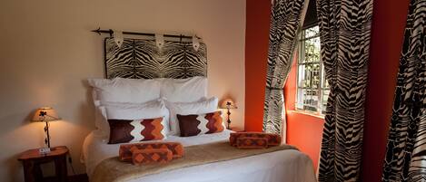 Ein Bett mit weißer Bettwäsche, zahlreichen Kissen, einem Zebra-Muster-Kopfstück und Vorhängen mit Zebra-Muster.