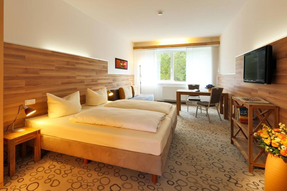 A modern hotel room with a large bed, a desk, and a television.
