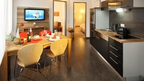 Una cocina moderna con armarios oscuros, un comedor con mesa y sillas de madera, y un televisor montado en la pared.