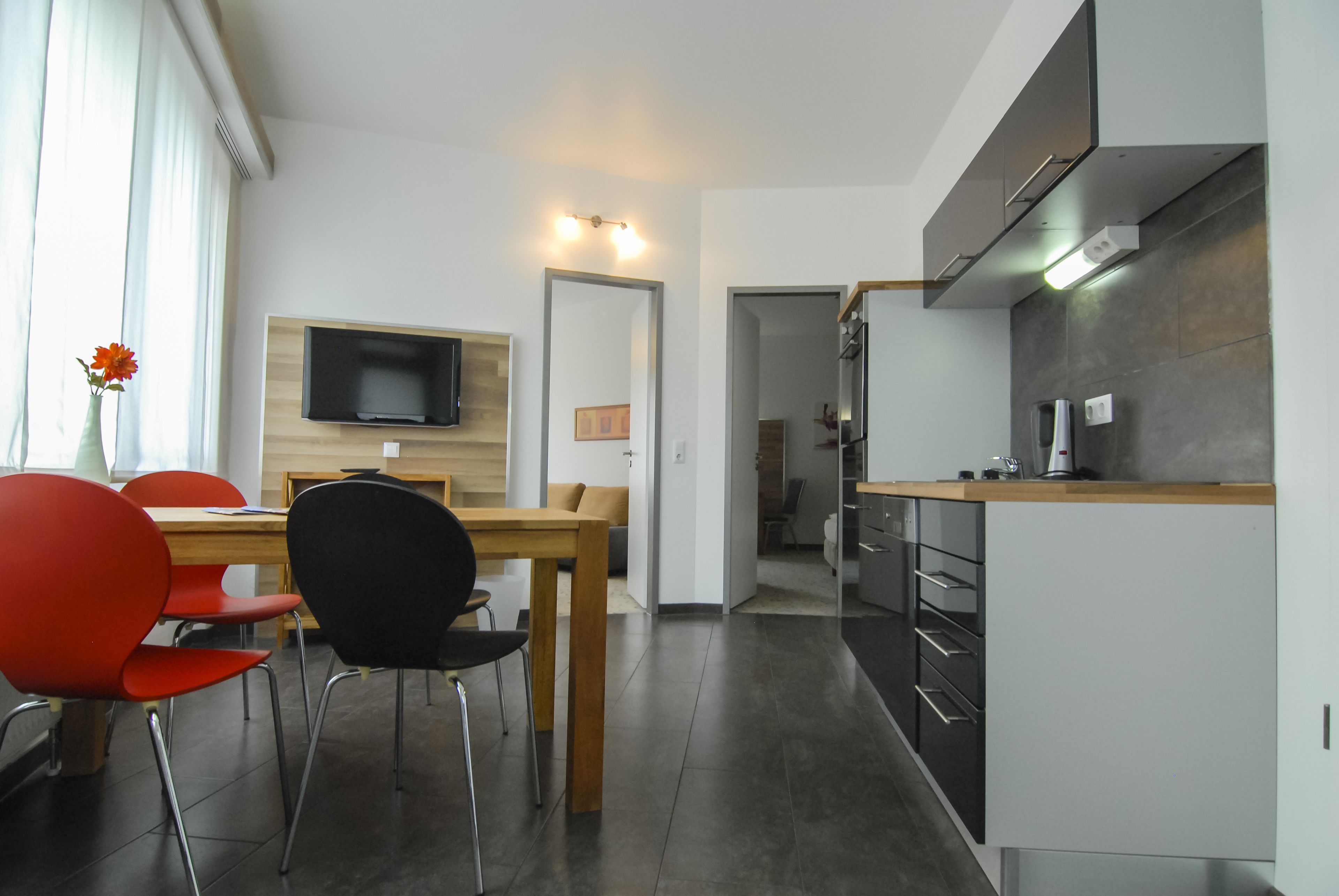 Una cocina moderna con una mesa y sillas de madera, un televisor empotrado y una isla de cocina con una cafetera.
