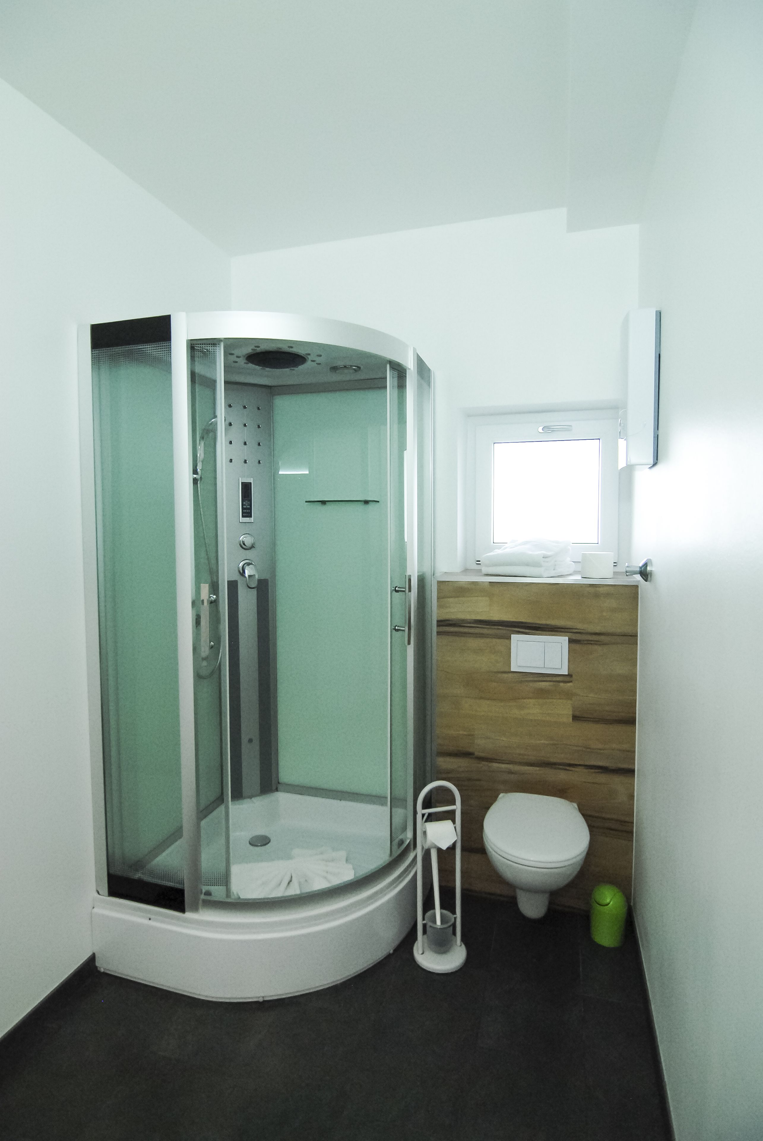 A modern bathroom with a glass-enclosed shower, a wooden vanity, a toilet, and a small window.