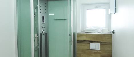 A modern bathroom with a glass-enclosed shower, a wooden vanity, a toilet, and a small window.