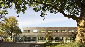 Un edificio moderno con fachada de vidrio, exterior de ladrillo y un gran árbol en la parte delantera.