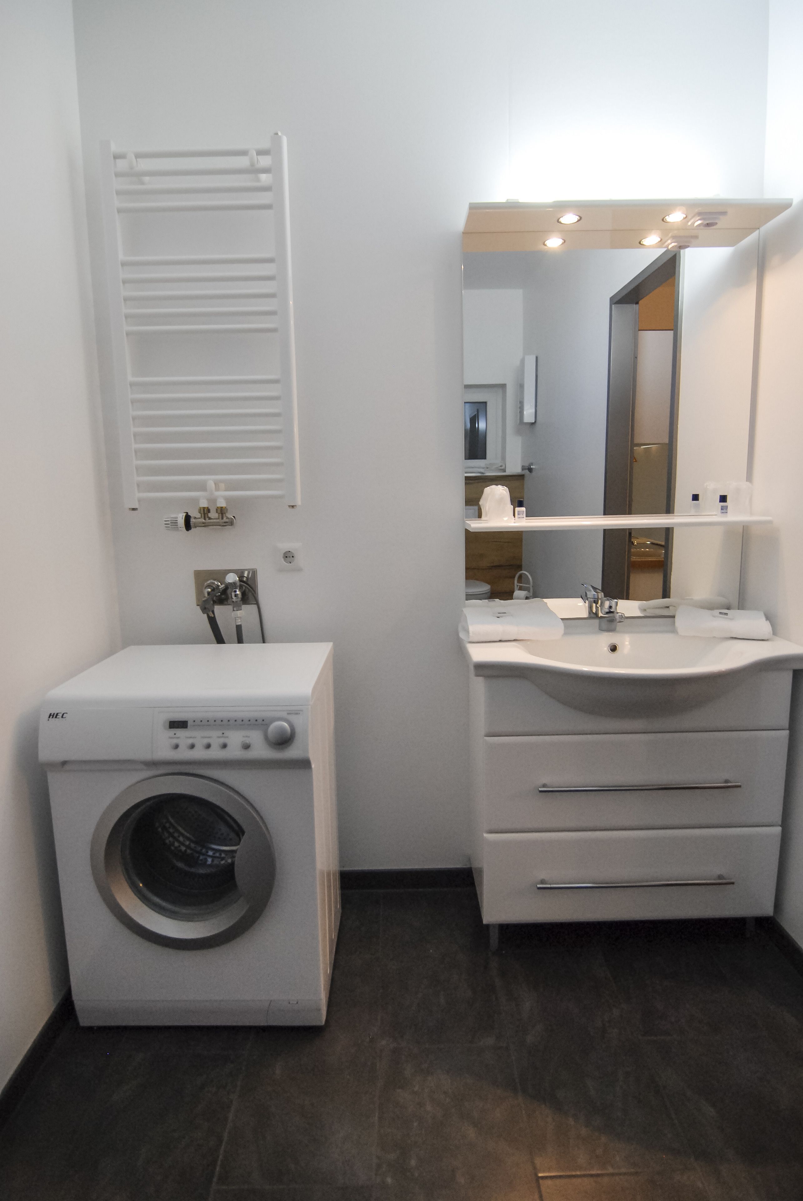 A compact bathroom with a washing machine, a sink, and a mirror.