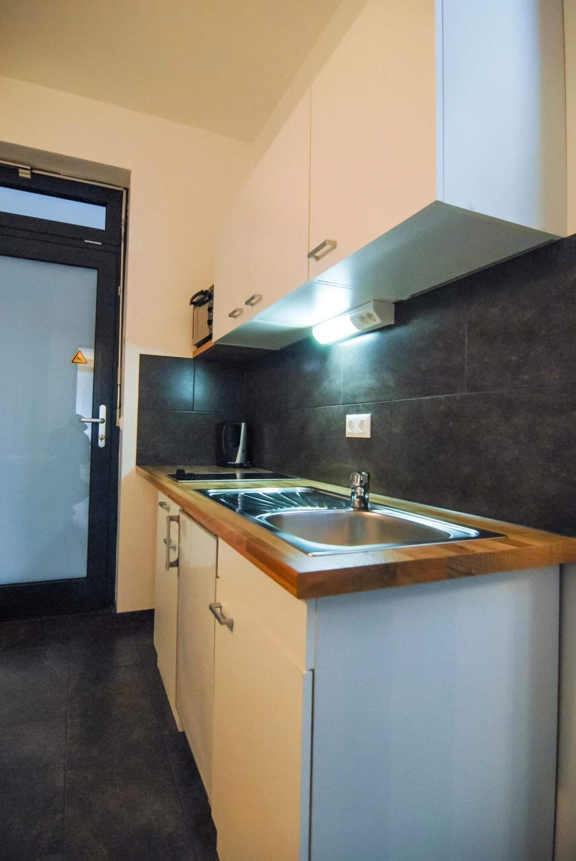 Een moderne keuken met een roestvrijstalen spoelbak, een donkere betegelde spatwand en een houten aanrecht.
