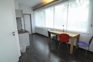 A small, modern room with a wooden desk and two chairs, a white radiator, and a window with sheer curtains. - Petul Apart Hotel Am Ruhrbogen (Bochum)