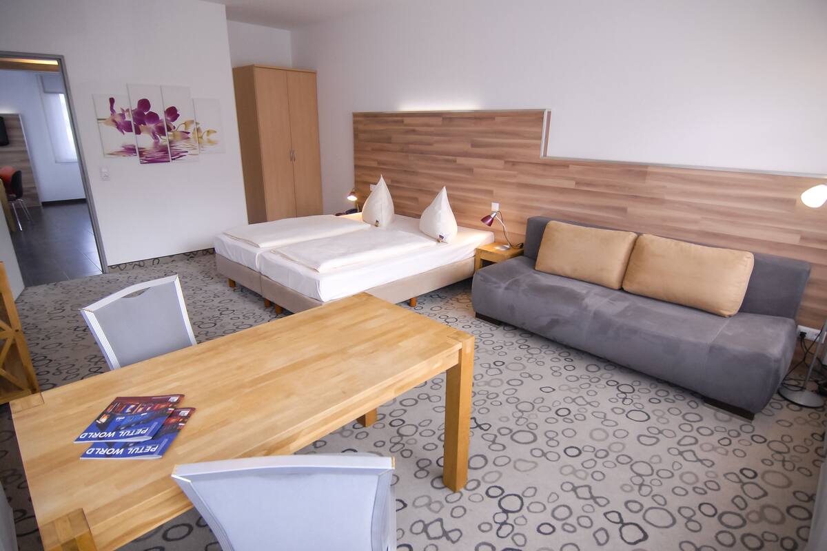 A hotel room with a bed, a sofa, a wooden table, and a patterned carpet.