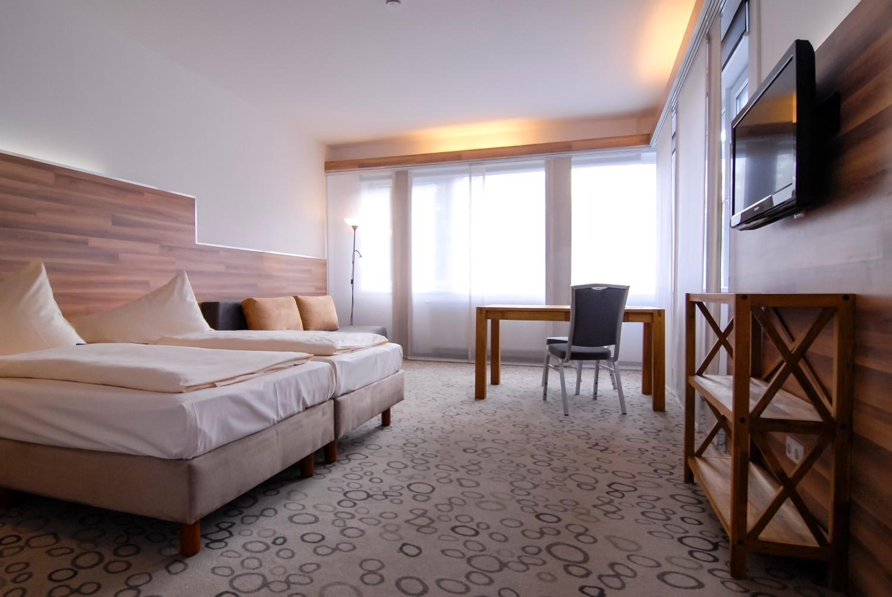 Ein Hotelzimmer mit einem Bett, einem Schreibtisch und einem an der Wand befestigten Fernseher.