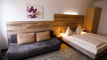 A bedroom with a wooden headboard, a grey sofa, a bed with white bedding, and a small bedside table with a lamp.